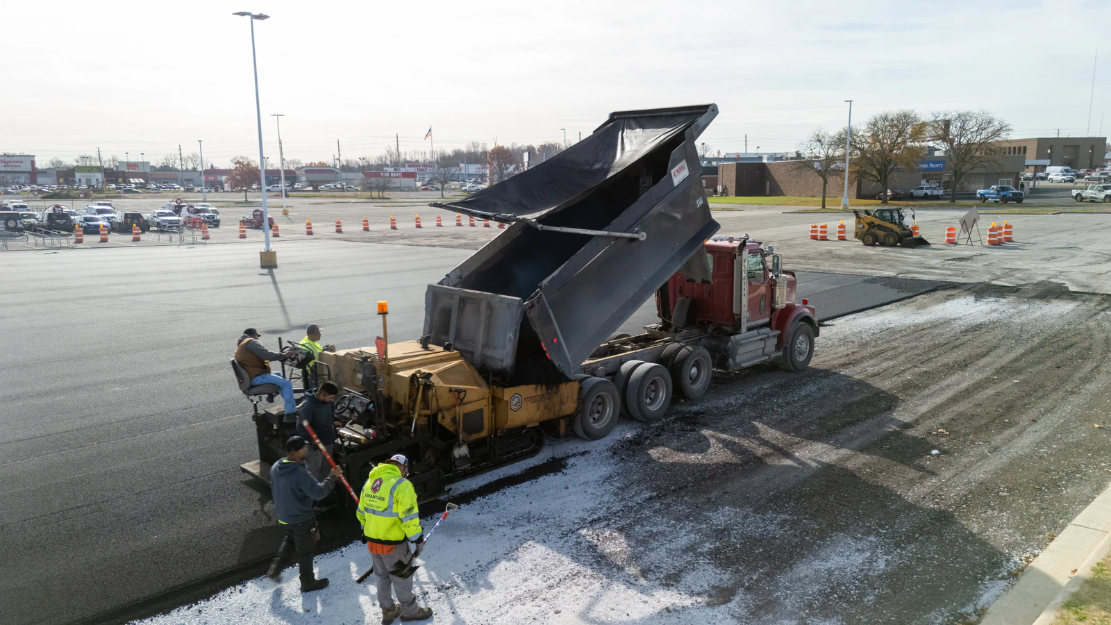 Dump truck feeding hot-mix asphalt into a paver as the Advantage Paving crew lays new pavement on a commercial lot